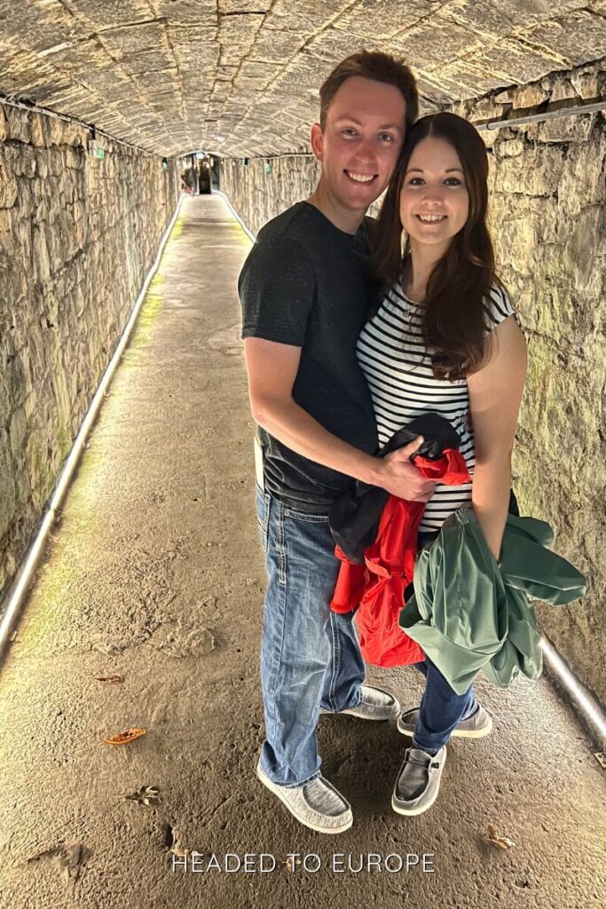 Tucker & Janae standing in a narrow stone tunnel with a vaulted ceiling and LED lights lining the floor edges, giving a cozy underground vibe.