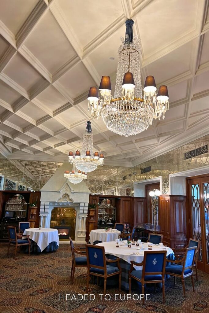 Elegant dining room at Ashford Castle featuring crystal chandeliers, white tablecloths, a grand fireplace, and mirrored walls creating a bright, upscale atmosphere.