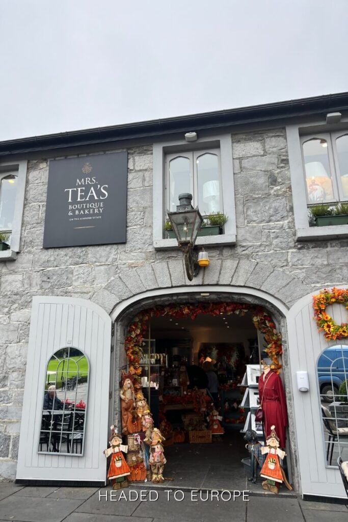 Exterior view of Mrs. Tea’s Boutique & Bakery at Ashford Estate, a stone building with arched doorways and festive autumnal decorations flanking the entrance.