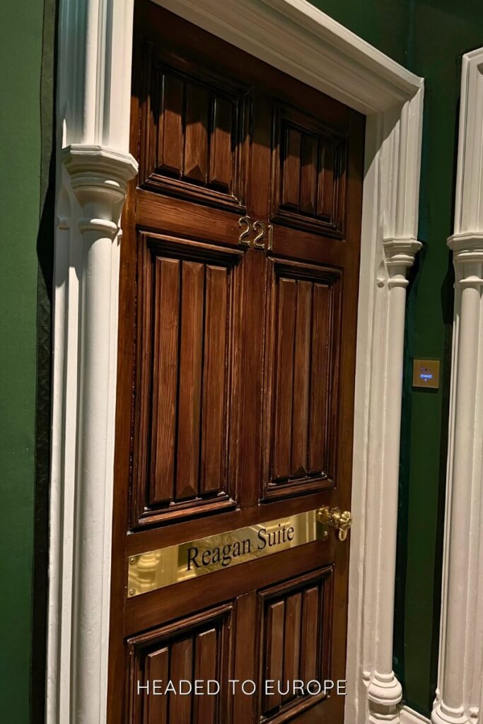 Wooden suite door in Ashford Castle labeled “221” with a gold nameplate reading “Reagan Suite,” framed by white decorative columns against a dark green wall.