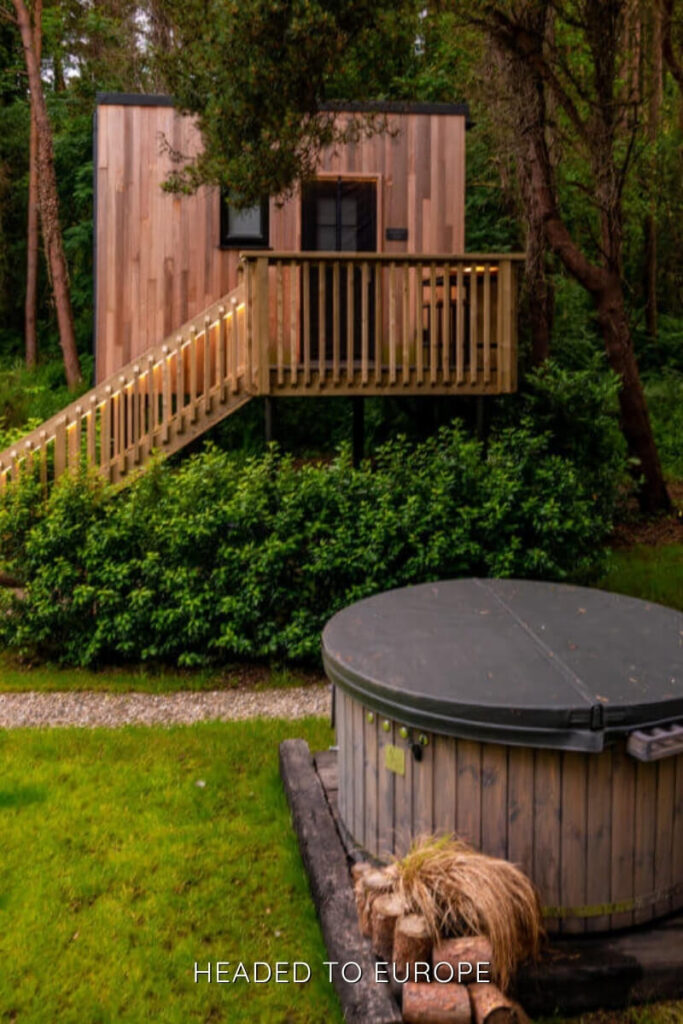A cozy wooden cabin in the forest with a private hot tub in the foreground, offering a secluded and relaxing escape for Weekend Breaks in Ireland.