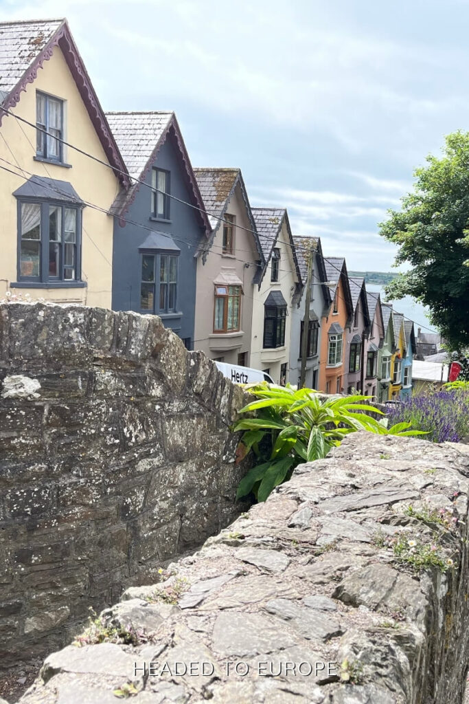 A row of colorful houses on a sloped street in Cobh overlooking the sea, capturing the vibrant charm of Weekend Breaks in Ireland.
