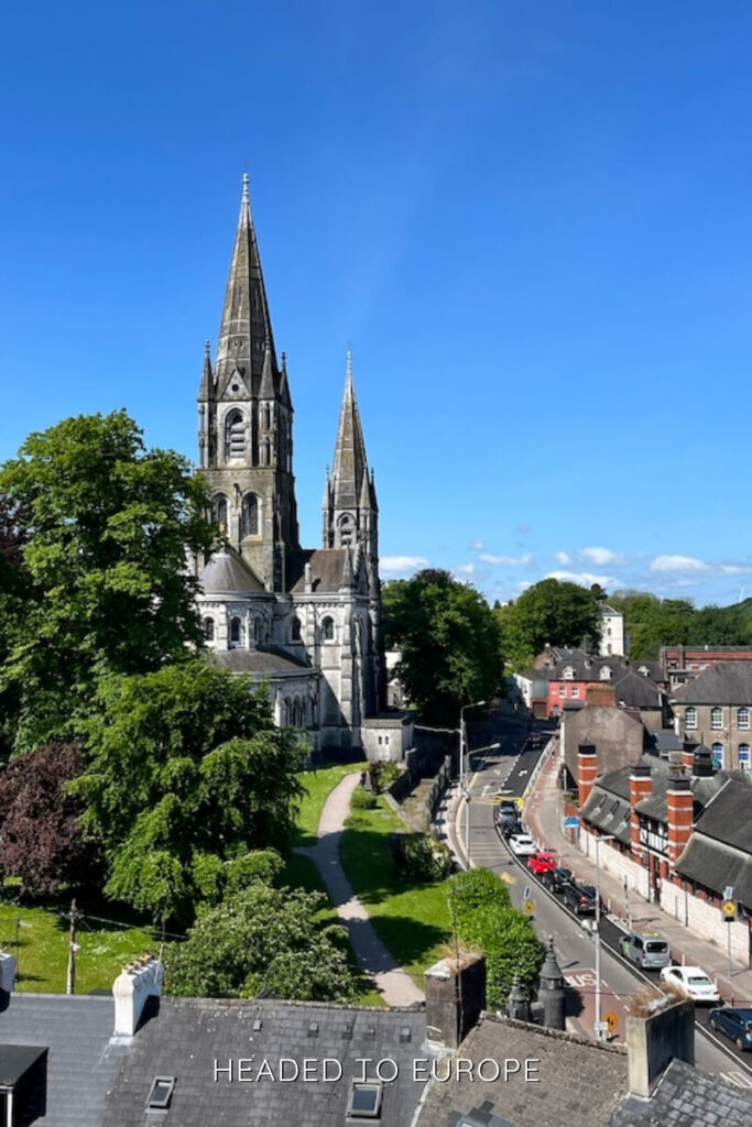 The twin spires of Saint Fin Barre’s Cathedral towering above lush greenery and classic Cork streets, a must-see on Weekend Breaks in Ireland.