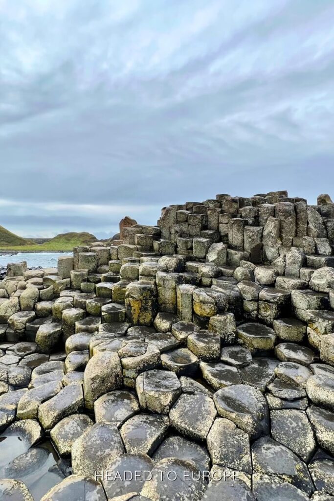 Hexagonal basalt columns at the Giant’s Causeway rise in uneven steps along the rugged shoreline, glistening slightly under overcast skies.
