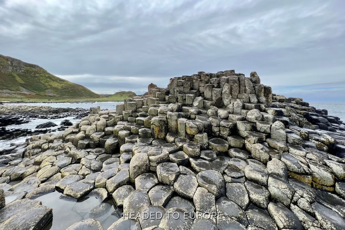 Hexagonal basalt columns at the Giant’s Causeway rise in uneven steps along the rugged shoreline, glistening slightly under overcast skies.