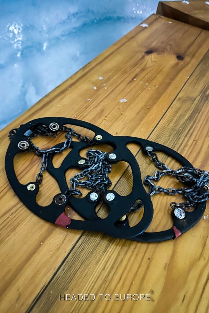 A pair of black rubber and metal crampons sit on a wooden bench, ready for use during the Into the Glacier tour. These traction devices help visitors safely walk on the slippery ice floors inside the glacier tunnels.