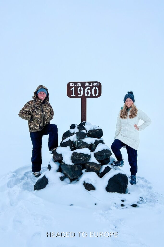 Janae and Tucker pose by a rock pile marker labeled “Iceline – Jökulrönd 1960” during their Into the Glacier adventure. The snowy landscape and minimal visibility emphasize the elevation and remoteness of the glacier's surface.