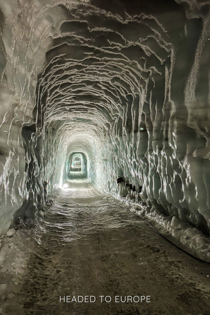 A long, arched tunnel inside Into the Glacier stretches forward with ribbed ice formations along the ceiling and walls. The pathway is illuminated by small lights, emphasizing the tunnel’s carved structure deep within the glacier.