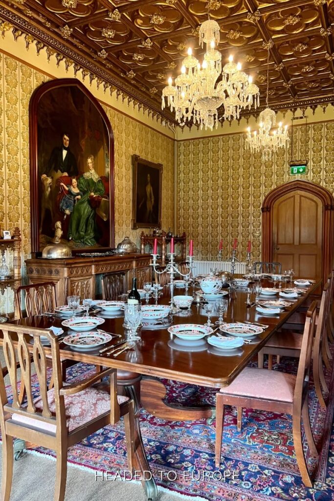 Ornate dining room inside an Irish castle, featuring a long wooden table set with fine china and crystal, surrounded by gold-accented wallpaper, chandeliers, and historic paintings.