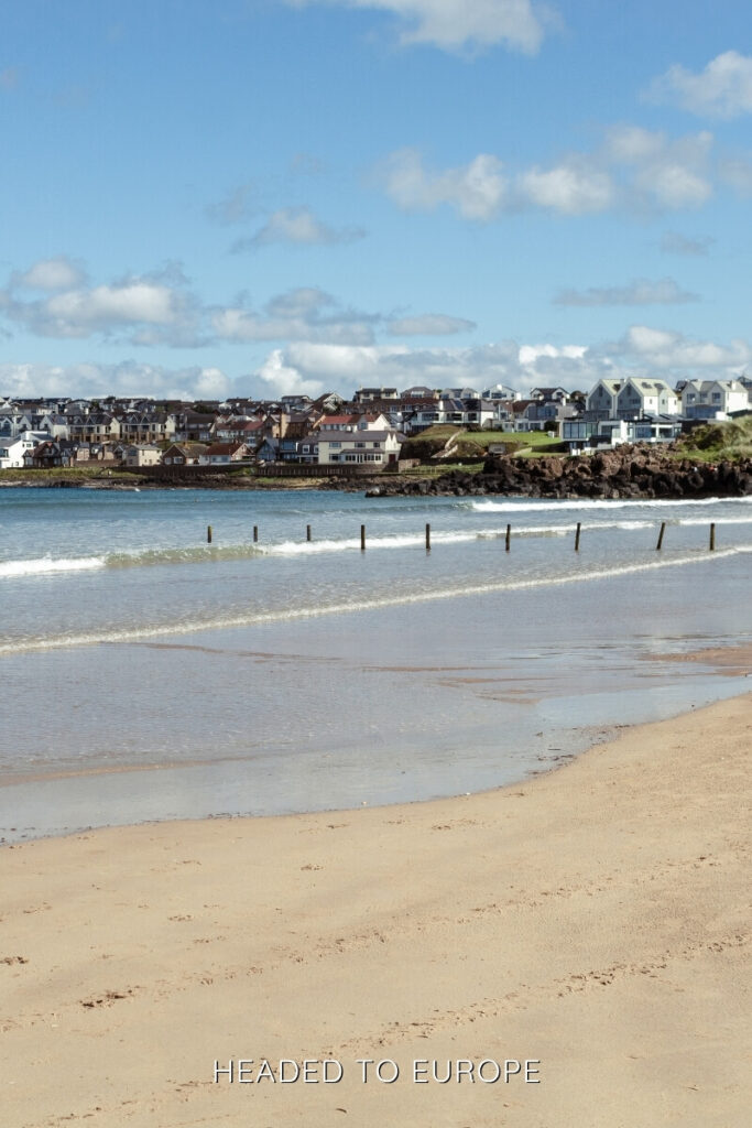 A sandy beach with gentle waves and a backdrop of coastal homes in Portstewart, perfect for seaside Weekend Breaks in Ireland.