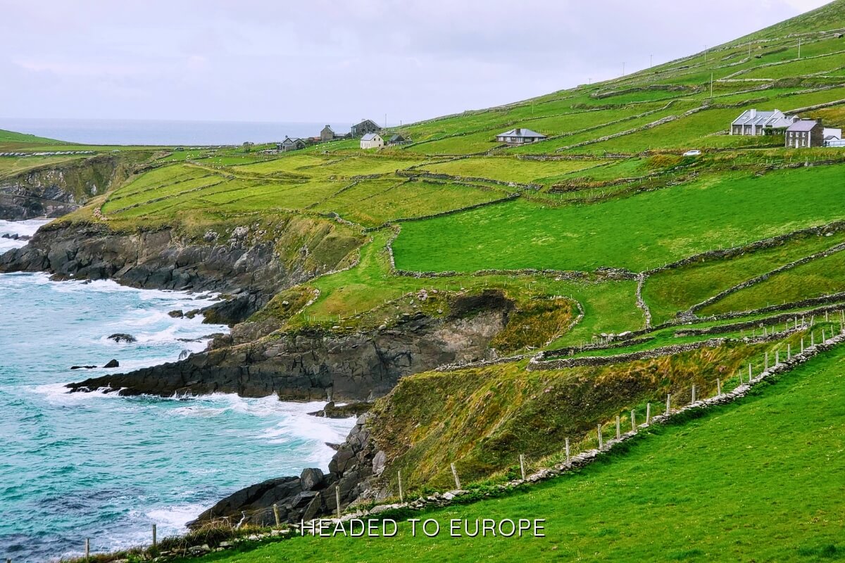 Green patchwork fields on rolling cliffs meet the Atlantic Ocean along Ireland’s western coastline, showcasing dramatic beauty on Weekend Breaks in Ireland.